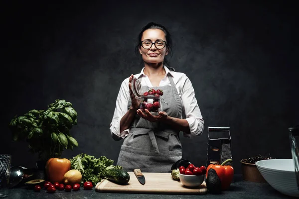 Bella cuoca di mezza età tiene un bicchiere con fragole fresche e succose in cucina — Foto Stock