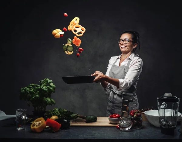 揚げパンから空気中に野菜のみじん切りを投げ幸せな中年女性シェフ — ストック写真