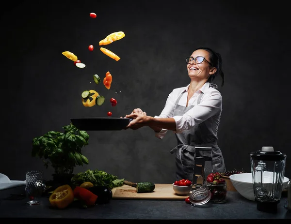 揚げパンから空気中に野菜のみじん切りを投げ幸せな中年女性シェフ — ストック写真