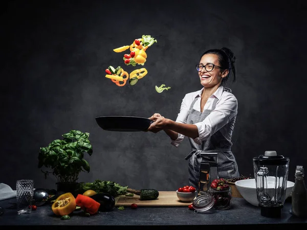 揚げパンから空気中に野菜のみじん切りを投げ幸せな中年女性シェフ — ストック写真