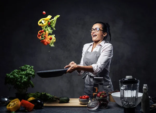 Bella donna matura che cucina insalata di verdure in cucina, getta le verdure dalla padella — Foto Stock