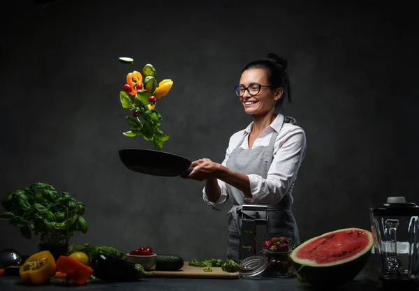 美しい成熟した女性キッチンで野菜サラダを調理し、パンから野菜をトス — ストック写真
