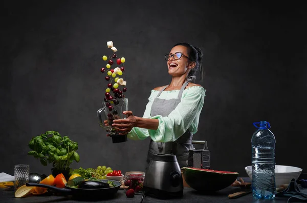 感情的に成熟した女性でエプロントス新鮮な果物で空気中からミキサーでキッチン — ストック写真