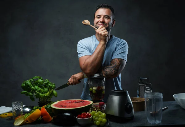 Bello tatuato maschio in camicia blu appoggiato su un frullatore in cucina — Foto Stock