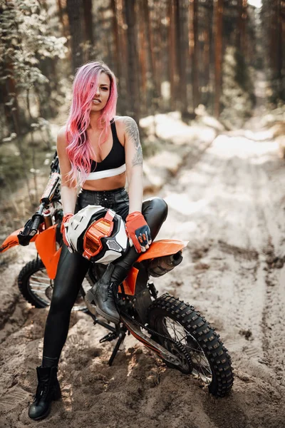 Moderna chica hipster tatuada con pelo rosa brillante sentada en su moto de motocross en el bosque —  Fotos de Stock