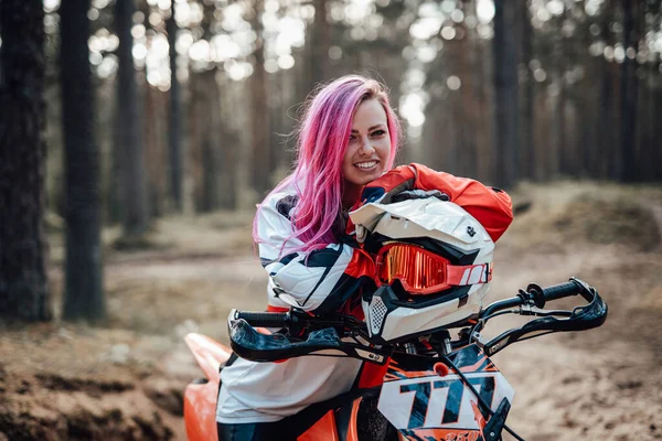 在越野赛中，身穿越野赛服、一头粉红头发的年轻赛车手女孩坐在摩托车上 — 图库照片