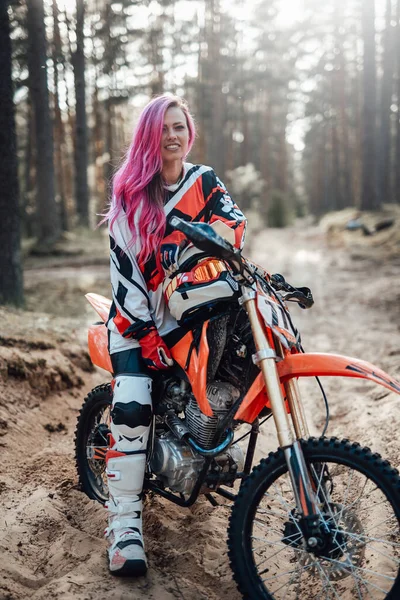 Młoda dziewczyna zawodnik z różowymi włosami w zestaw motocross siedzi na jej motocyklu w off road przygody — Zdjęcie stockowe