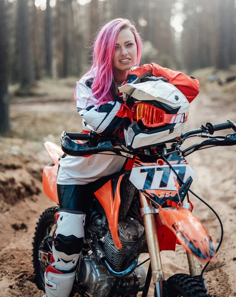 Młoda dziewczyna zawodnik z różowymi włosami w zestaw motocross siedzi na jej motocyklu w off road przygody — Zdjęcie stockowe