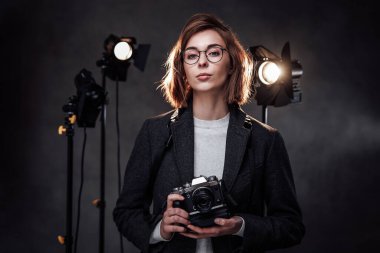 Güzel kızıl saçlı kadın fotoğrafçı elinde dijital kamerayla kameraya bakıyor.