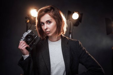 Güzel kızıl saçlı kadın fotoğrafçı elinde dijital kamerayla kameraya bakıyor.