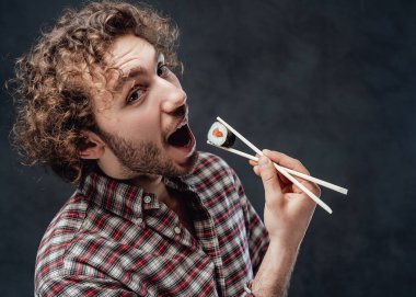 Kıvırcık saçlı, duygusal yakışıklı bir adam yemek çubuklarını elinde tutuyor ve kameraya bakıyor.