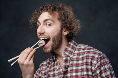 Kıvırcık saçlı, duygusal yakışıklı bir adam yemek çubuklarını elinde tutuyor ve kameraya bakıyor.