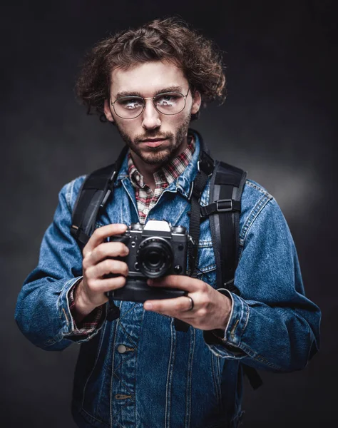 Retrato de un joven fotógrafo guapo con el pelo rizado usando chaqueta de mezclilla sostiene una cámara —  Fotos de Stock