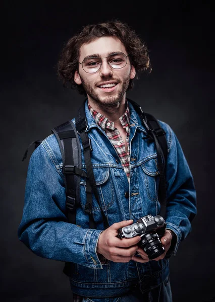 Portrait d'un beau jeune photographe aux cheveux bouclés portant une veste en denim tient un appareil photo — Photo