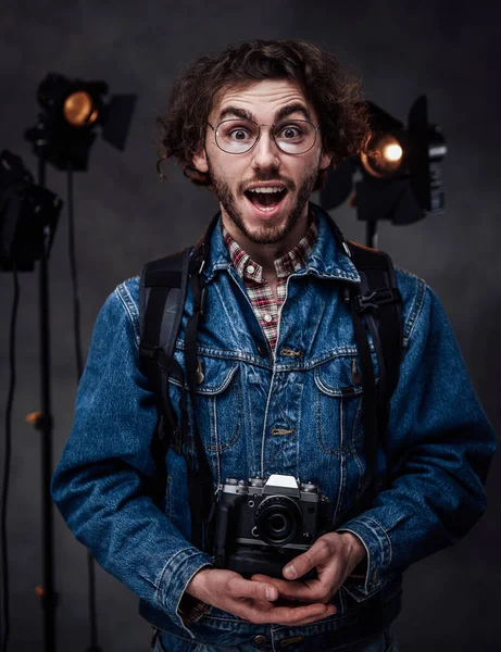 Jovem fotógrafo segura uma câmera. Retrato de estúdio com equipamento de iluminação em segundo plano — Fotografia de Stock