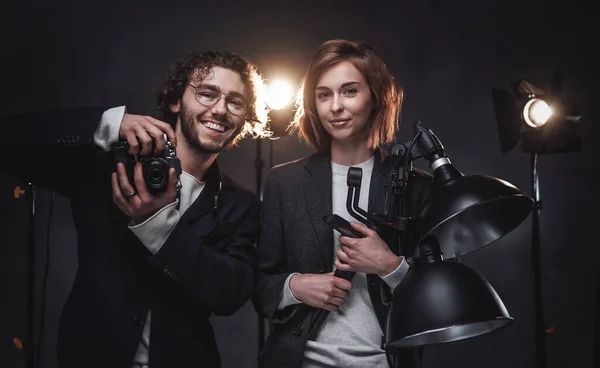 El equipo de dos fotógrafos sostiene una cámara digital y un equipo de iluminación posando en el estudio — Foto de Stock