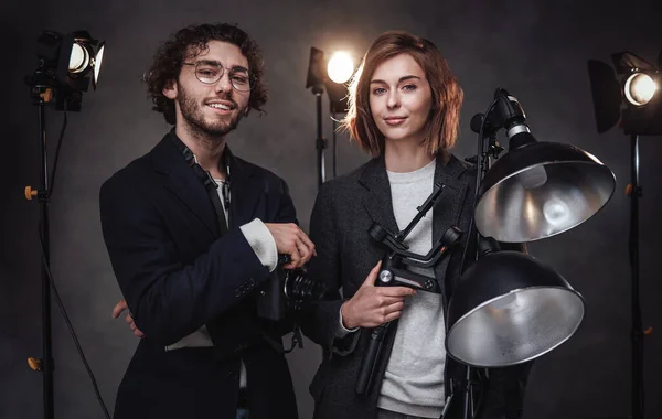 El equipo de dos fotógrafos sostiene una cámara digital y un equipo de iluminación posando en el estudio — Foto de Stock