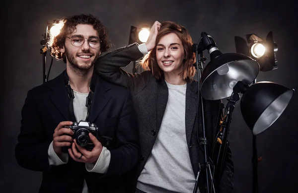 The team of two photographers holds a digital camera and lighting equipment posing in studio — Stock Photo, Image