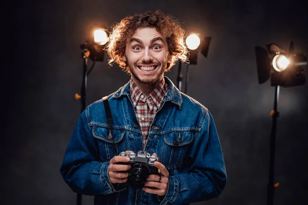 El joven fotógrafo sostiene una cámara. Retrato de estudio con equipo de iluminación en el fondo — Foto de Stock