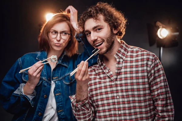 Hermosa joven pareja de moda disfruta de deliciosos rollos de sushi en estudio oscuro — Foto de Stock