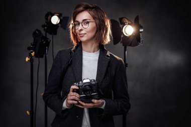 Güzel kızıl saçlı kadın fotoğrafçı elinde dijital kamerayla kameraya bakıyor.