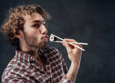 Kıvırcık saçlı, duygusal yakışıklı bir adam yemek çubuklarını elinde tutuyor ve kameraya bakıyor.