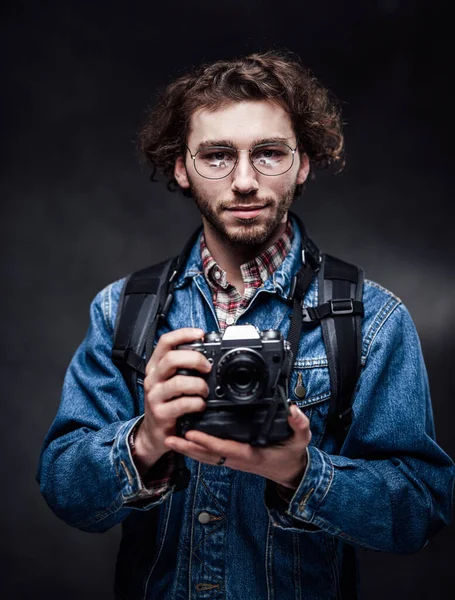 Retrato de um jovem fotógrafo bonito com cabelo encaracolado usando jaqueta de ganga segura uma câmera — Fotografia de Stock