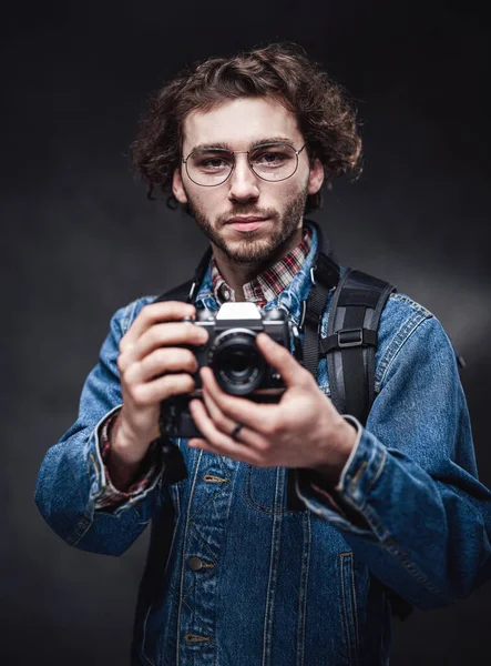 Retrato de un joven fotógrafo guapo con el pelo rizado usando chaqueta de mezclilla sostiene una cámara — Foto de Stock