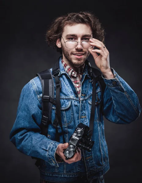 Portrét pohledného mladého fotografa s kudrnatými vlasy v džínové bundě drží fotoaparát — Stock fotografie