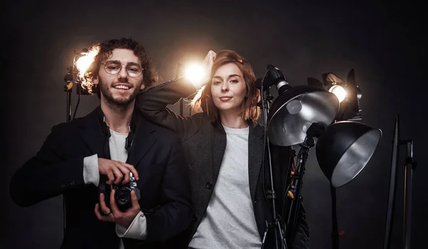 Команда из двух фотографов держит цифровую камеру и световое оборудование, позирующее в студии — стоковое фото