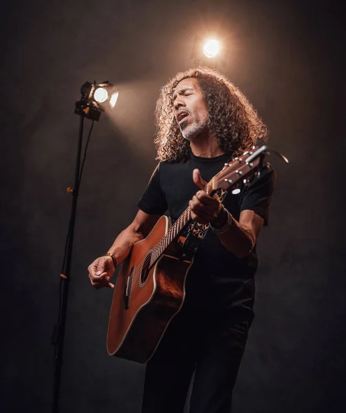Músico hispânico de meia-idade em t-shirt preta emocionalmente cantando e tocando guitarra — Fotografia de Stock