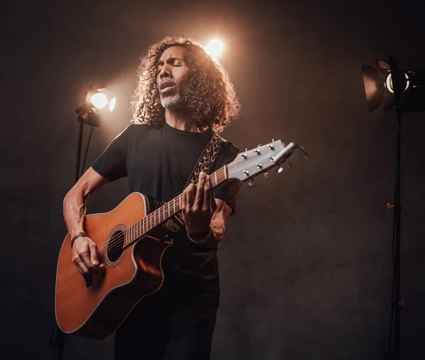 Músico hispânico de meia-idade em t-shirt preta emocionalmente cantando e tocando guitarra — Fotografia de Stock