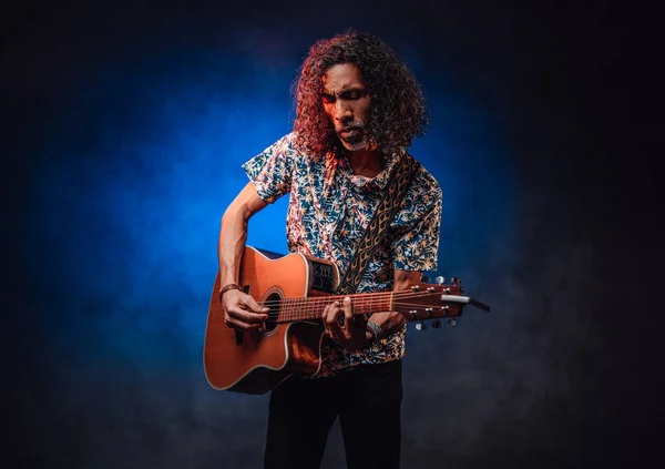 Talangfull latinamerikansk musiker i en hawaiiansk skjorta som spelar gitarr på en mörk — Stockfoto