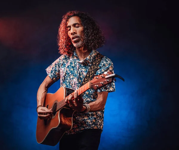 Talented hispanic musician in a hawaiian shirt playing guitar on a dark — Stock Photo, Image