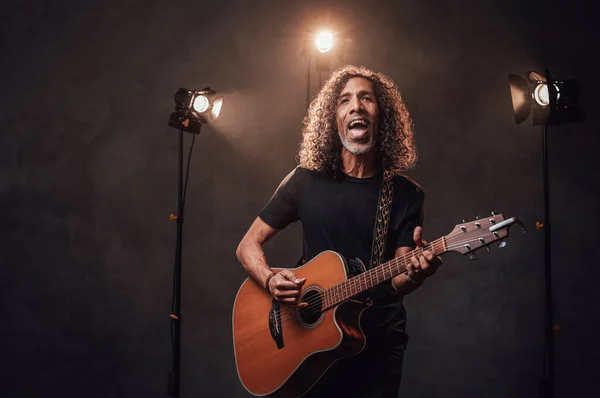 Músico hispânico de meia-idade em t-shirt preta emocionalmente cantando e tocando guitarra — Fotografia de Stock