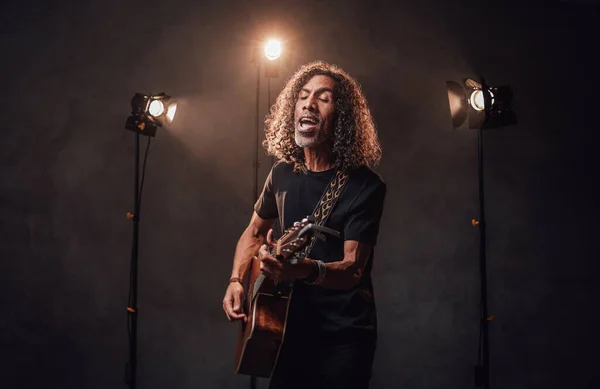 Middle aged hispanic musician in black t-shirt emotionally singing and playing guitar — Stock Photo, Image