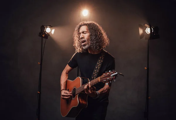 Middle aged hispanic musician in black t-shirt emotionally singing and playing guitar — Stock Photo, Image