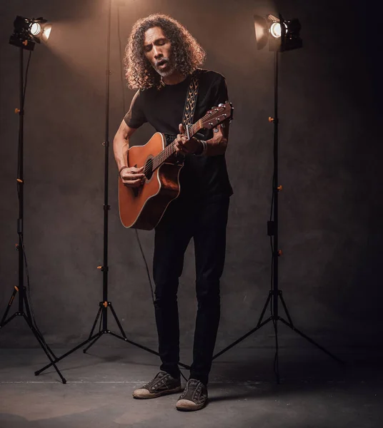 Full-length portrait of a hispanic musician emotionally playing guitar. View of musician in the spotlight — Stock Photo, Image