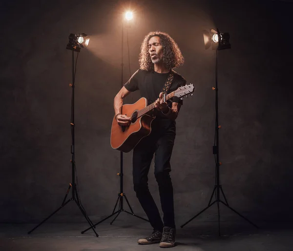 Full-length portrait of a hispanic musician emotionally playing guitar. View of musician in the spotlight — Stock Photo, Image