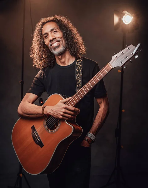 Middle aged hispanic man musician in black t-shirt holds guitar on a scene, smiling and looking on camera — Stock Photo, Image