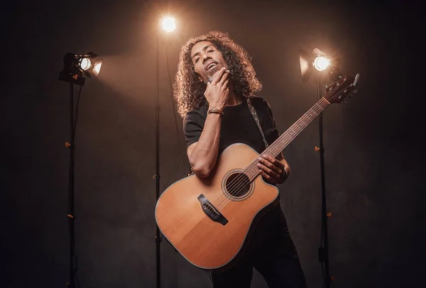 Homem hispânico de meia-idade músico em t-shirt preta detém guitarra em uma cena — Fotografia de Stock