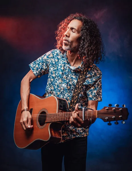 Talentoso músico hispânico com uma camisa havaiana tocando guitarra em um escuro — Fotografia de Stock