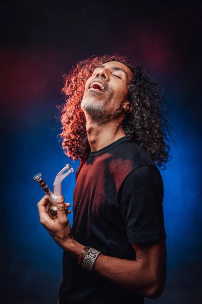 Middelbare leeftijd Spaanse man roken van bong op een donkere achtergrond verlicht blauw licht — Stockfoto