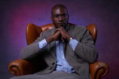 Lüks bir deri koltukta oturan kendine güvenen Afro-Amerikan işadamı dalgın görünüyor.