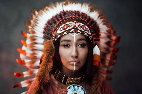 Ritratto ravvicinato di una giovane attraente donna indiana americana con trucco in cappello e vestiti di piume tradizionali — Foto Stock
