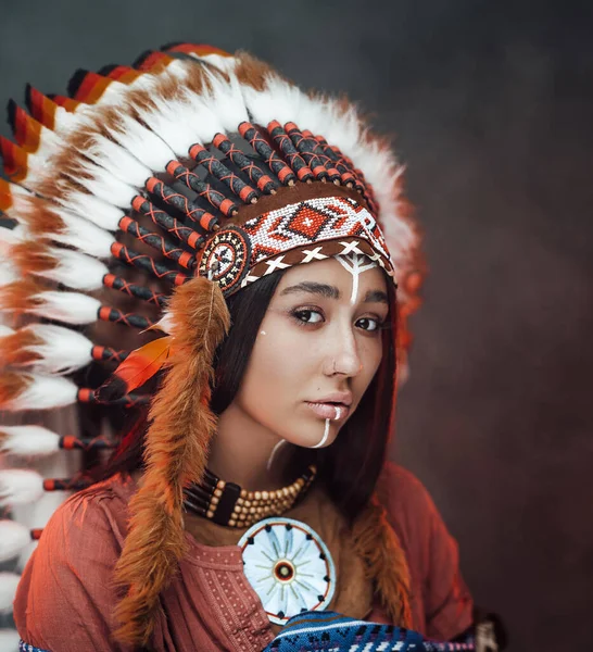 Close up portrait of a attractive young American Indian woman with make up in traditional feather hat and clothes — Stock Photo, Image