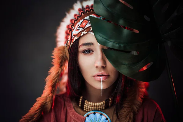 Beautiful young American Indian woman in ethnic costume holds a large green tropical leaf — Stock Photo, Image