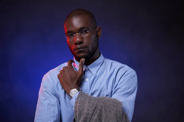 Africký americký podnikatel v modré košili a brýlích, vypadá zamyšleně a dívá se na kameru — Stock fotografie