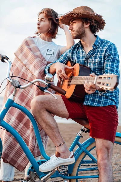 Unga män på cykeln med sin gitarr och en flicka insvept i en rosa filt bakom sig — Stockfoto