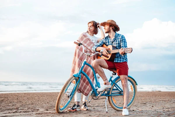 Två personer står med sin cykel. Pojken spelar på gitarr, bär fin hatt — Stockfoto